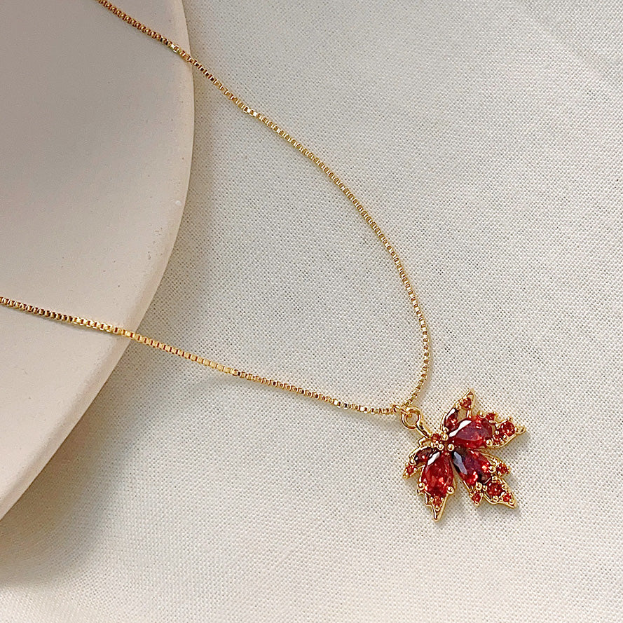 A stunning gold-plated choker necklace featuring a detailed maple leaf pendant set with brilliant red zircon crystals, on a clean white background.