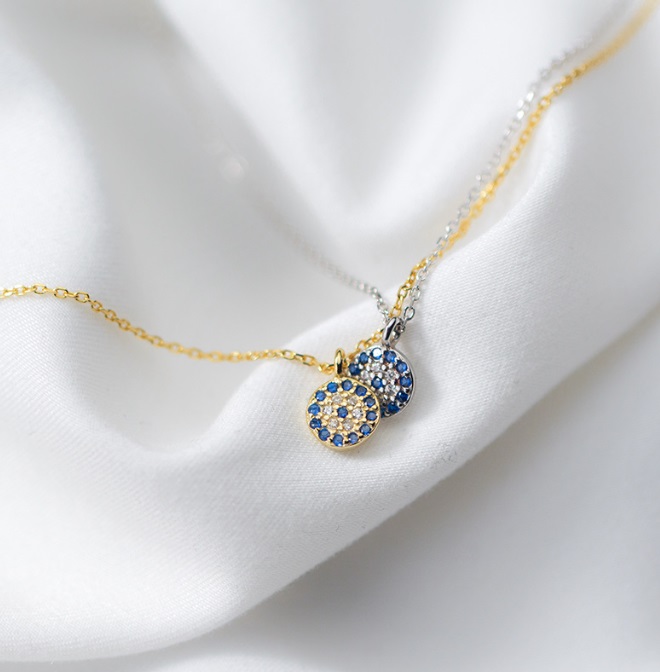 A close-up of the 925 Sterling Silver Evil Eye Pendant Necklace in a gold finish, featuring a circular pendant with sparkling blue and white cubic zirconia stones.