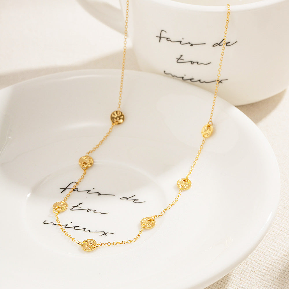 A set of gold-colored stainless steel choker necklaces with tiny hammered coin disc charms, elegantly displayed on a decorative dish.