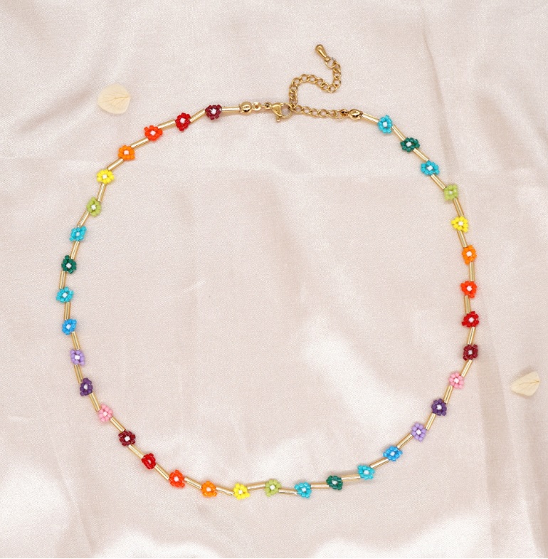Close-up of the Beaded Flower Necklace JRN-069, showcasing its gold chain and vibrant, colorful flower-shaped beads on a light pink fabric background.