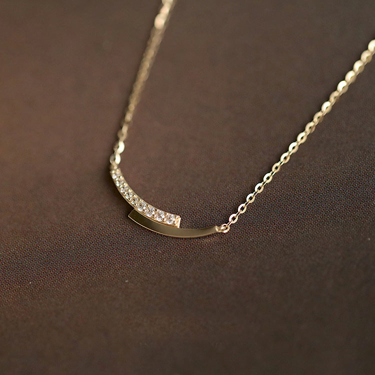 A close-up of a 925 sterling silver necklace from the pavé crystal set, featuring a gold finish and a distinctive curved pendant with sparkling crystals.