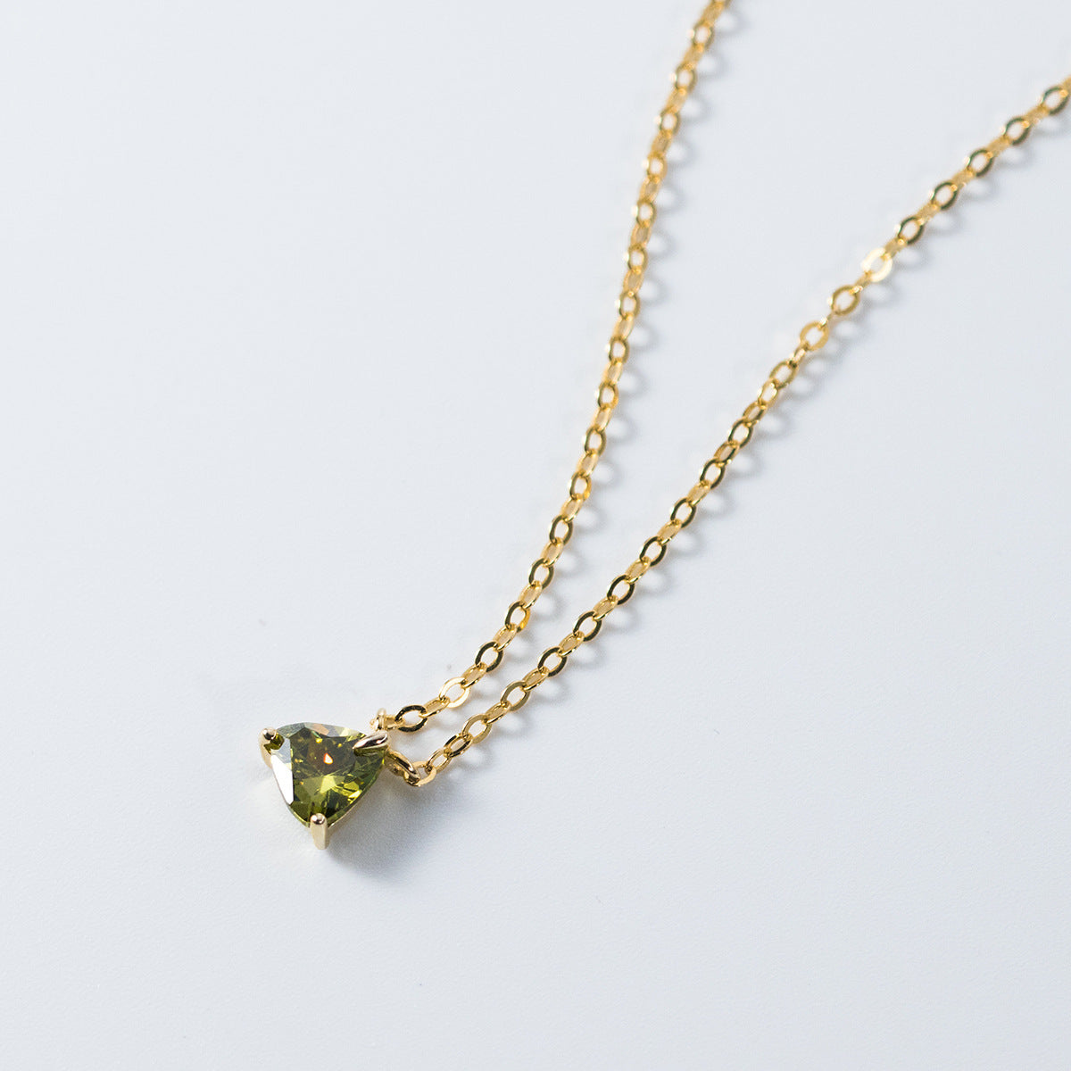 A close-up of a delicate gold-plated 925 sterling silver necklace featuring a triangular pendant with a brilliant green cubic zirconia stone.