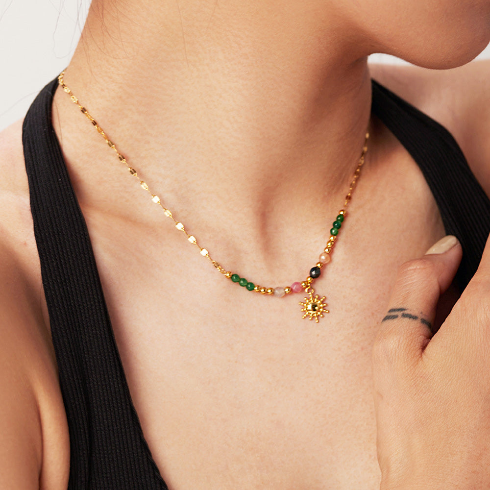 A close-up of a gold-plated stainless steel necklace with a radiant sun pendant, part of a French-style set with natural stone beads.
