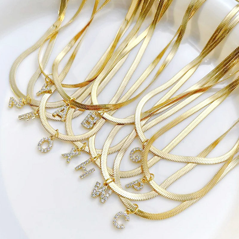 A collection of stainless steel gold-colored snake chain necklaces, each featuring a sparkling pave A-Z initial letter pendant.