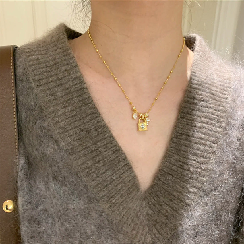 A close-up of a gold-plated brass chain necklace featuring a stylish padlock pendant with zircon accents, offered by JR Fashion Accessories for wholesale.