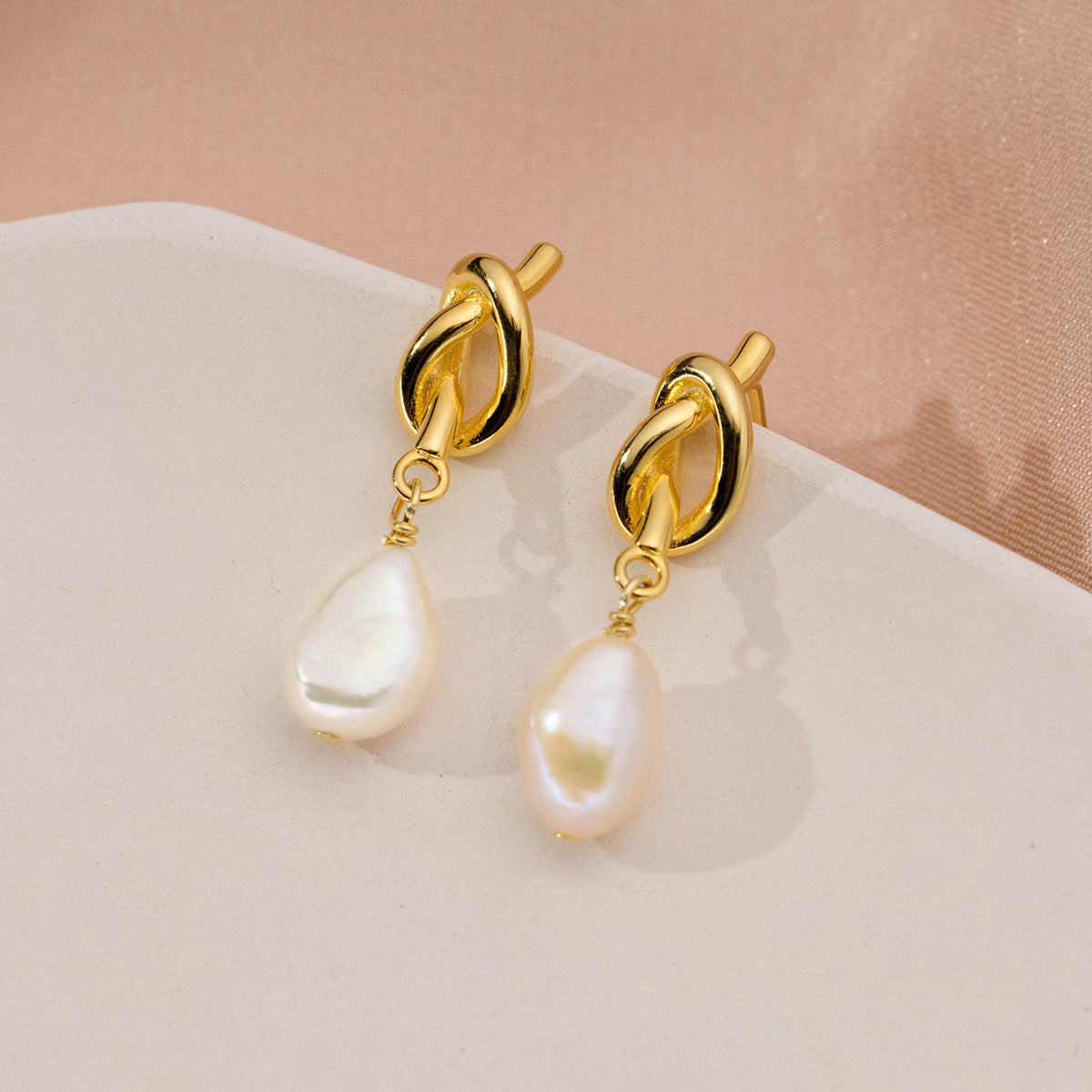 A pair of 18k gold-plated 925 sterling silver earrings featuring a vintage knot design and elegant white pearl drops.