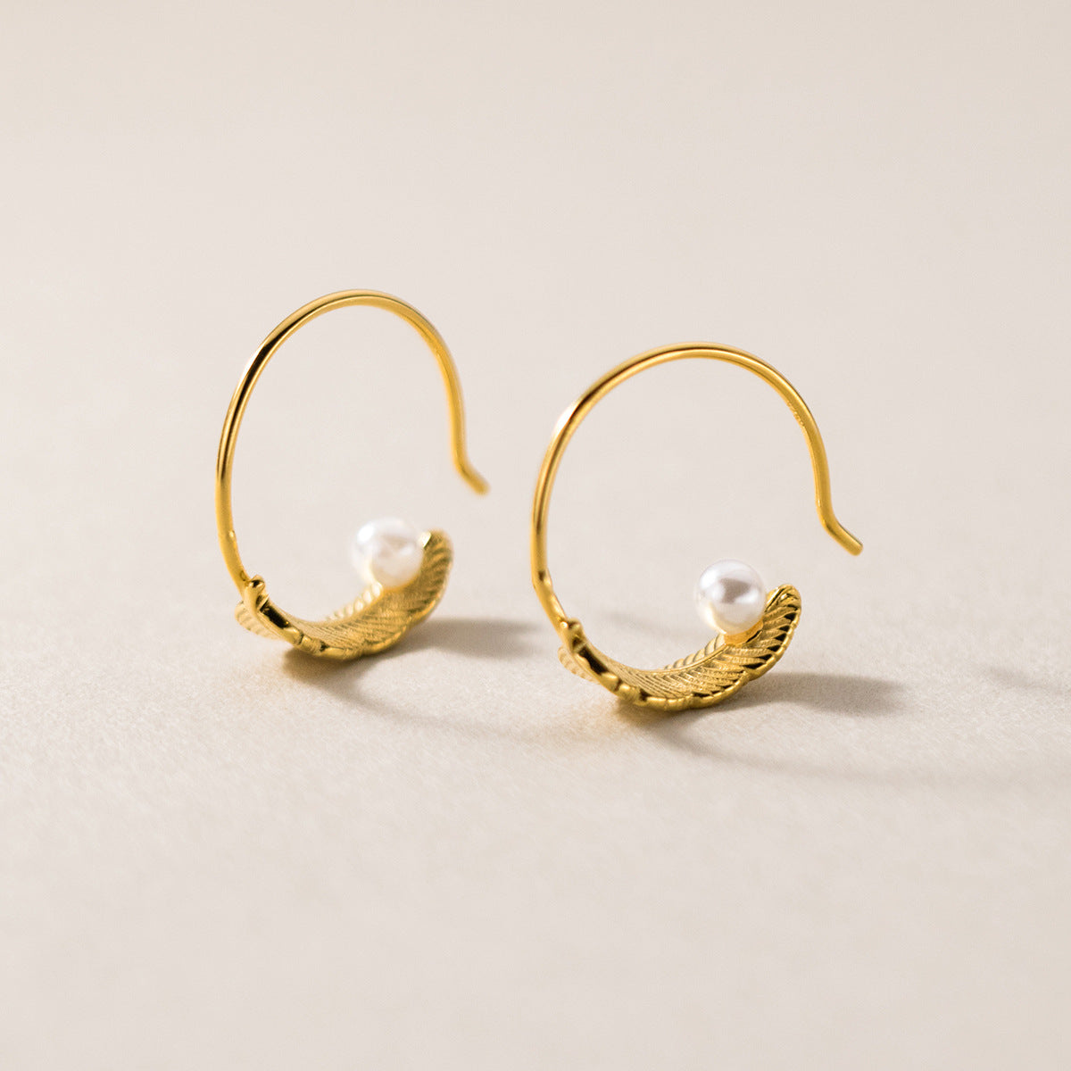 A close-up of a 925 sterling silver C-hoop stud earring with gold plating, featuring a textured feather design and a single white pearl accent.