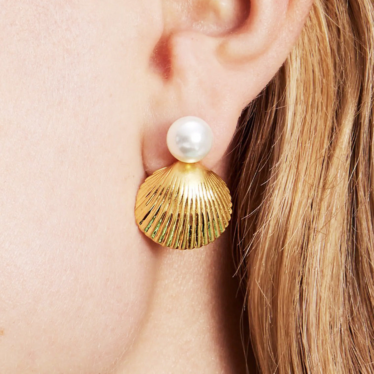 A close-up of a stainless steel gold shell-shaped stud earring featuring a single elegant pearl, showcasing its detailed design and lustrous finish.