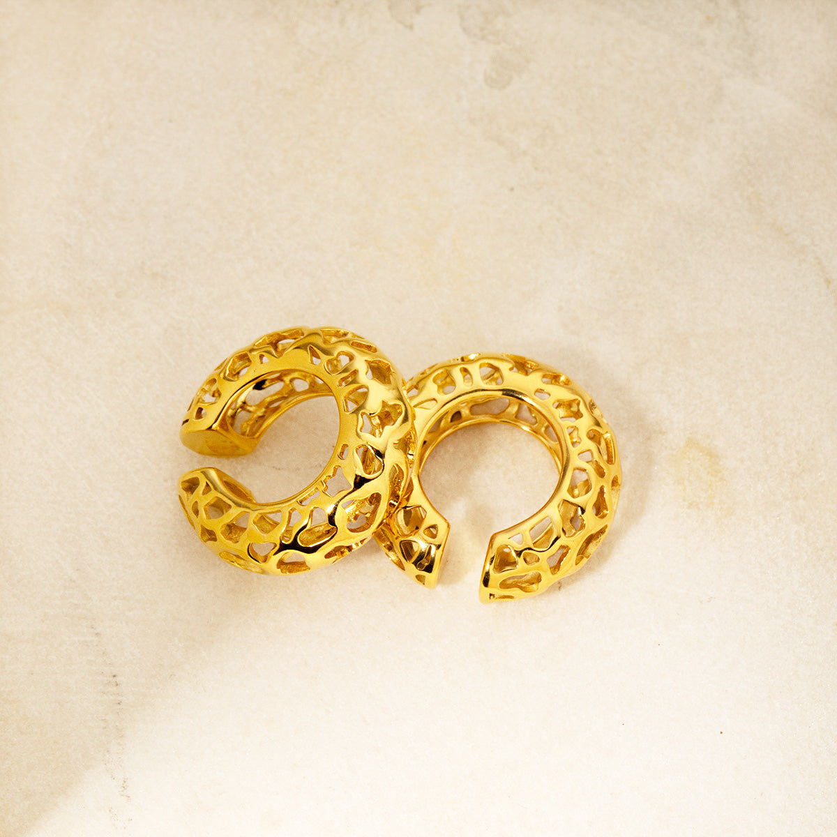 A pair of stainless steel gold-plated chunky ear cuff earrings with a unique hollow and perforated design.