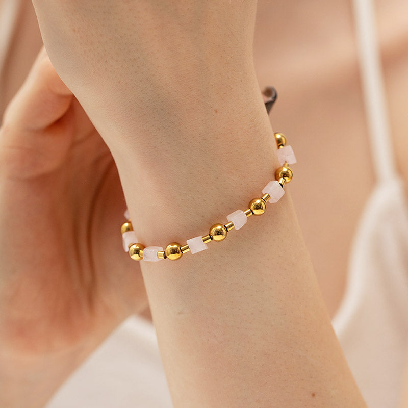 A woman's wrist adorned with an elegant stainless steel bracelet featuring natural pink stone beads and a delicate gold chain.