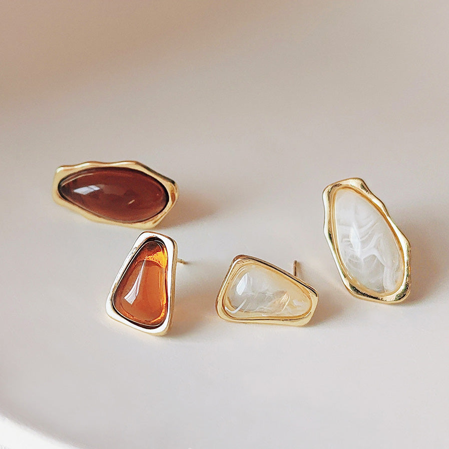 A collection of 14k gold-plated asymmetric stud earrings showcasing various translucent stone shapes and colors in gold settings.