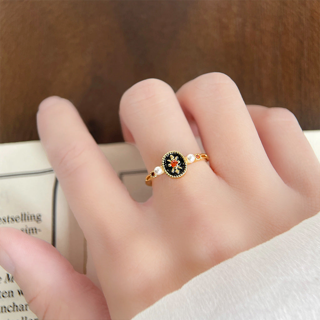 A detailed view of a retro 14k gold plated ring from the five-piece set, featuring a black enamel flower design and delicate pearl accents.