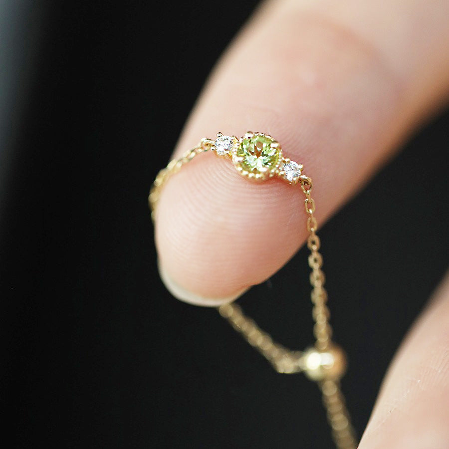 A close-up of an adjustable 925 sterling silver chain ring with a gold finish, featuring a brilliant olive-green cubic zirconia centerpiece.