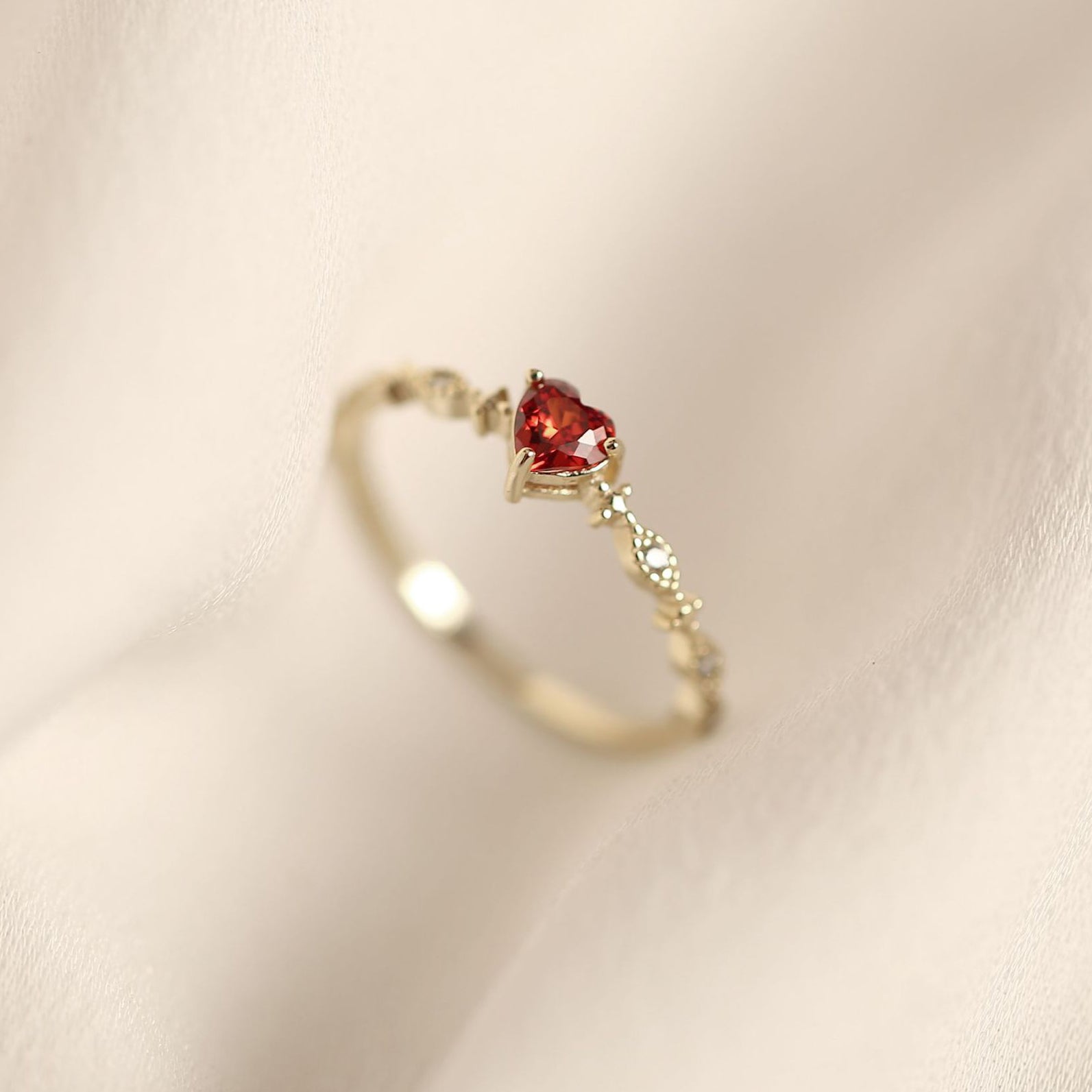 A close-up of a 925 sterling silver ring with a gold finish, featuring a brilliant heart-shaped red ruby at its center, from JR Fashion Accessories.