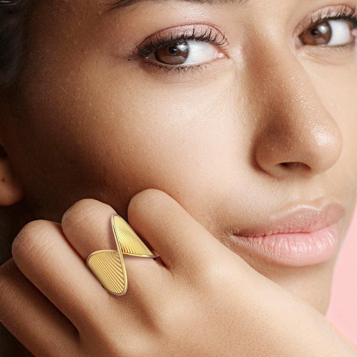A close-up of a woman's hand wearing an elegant gold-finished stainless steel ring with a geometric twist design.