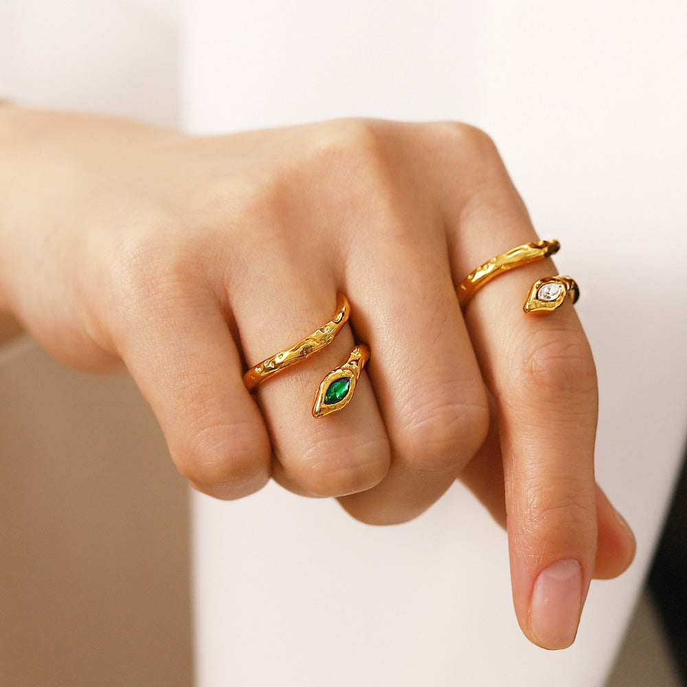 A model's hand wearing a set of four stainless steel gold-plated snake rings with white and green zircon gemstones.
