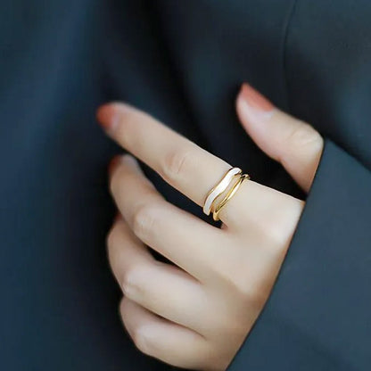 A woman's hand wearing the 14k gold-plated white enamel wave adjustable rings, showcasing their elegant design.