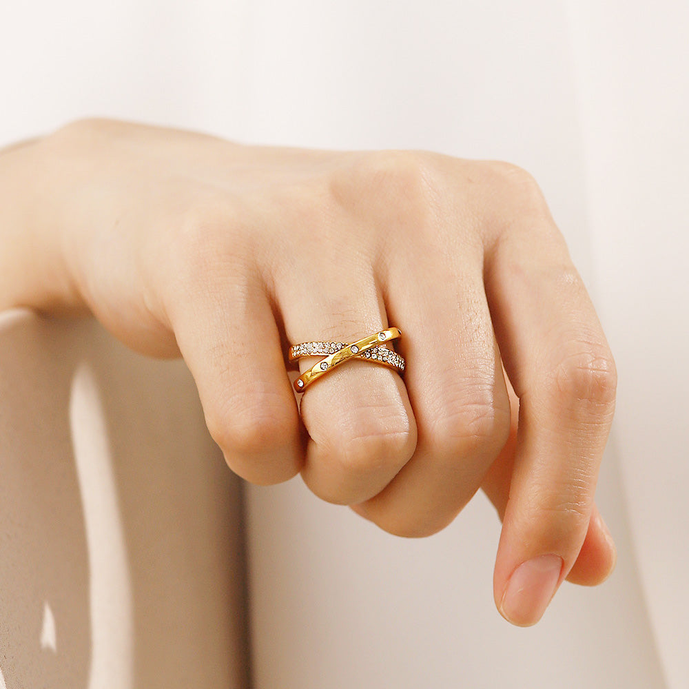 A close-up of a hand wearing a set of stainless steel gold-plated open rings with zircon cross and crisscross designs.