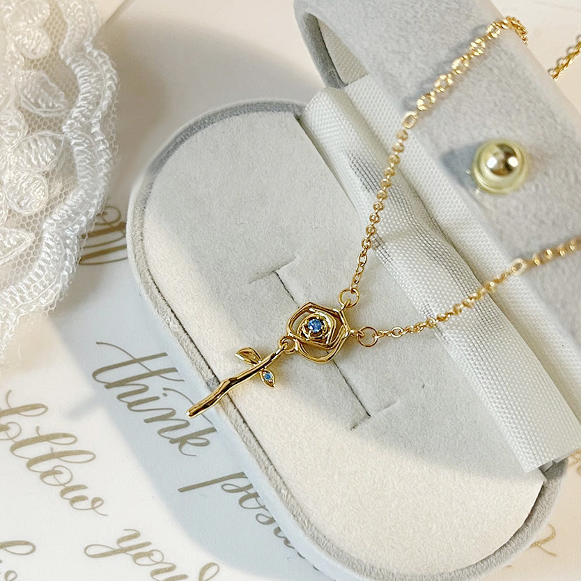 A stunning gold-plated rose flower pendant necklace with blue zirconia, part of a set of five, elegantly displayed on a white bust.