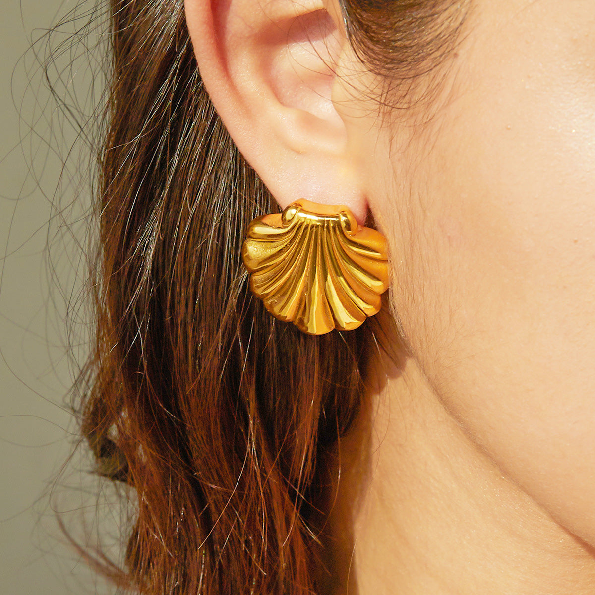 A detailed close-up of a gold-tone scallop shell stud earring, showcasing its textured surface and shiny finish. The earring is made from waterproof stainless steel, perfect for beach-themed jewelry.