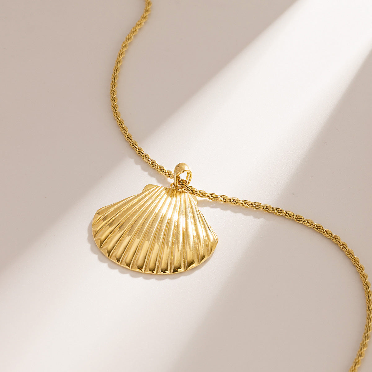 A close-up of a gold-plated stainless steel necklace featuring a detailed seashell pendant, on a clean white background.