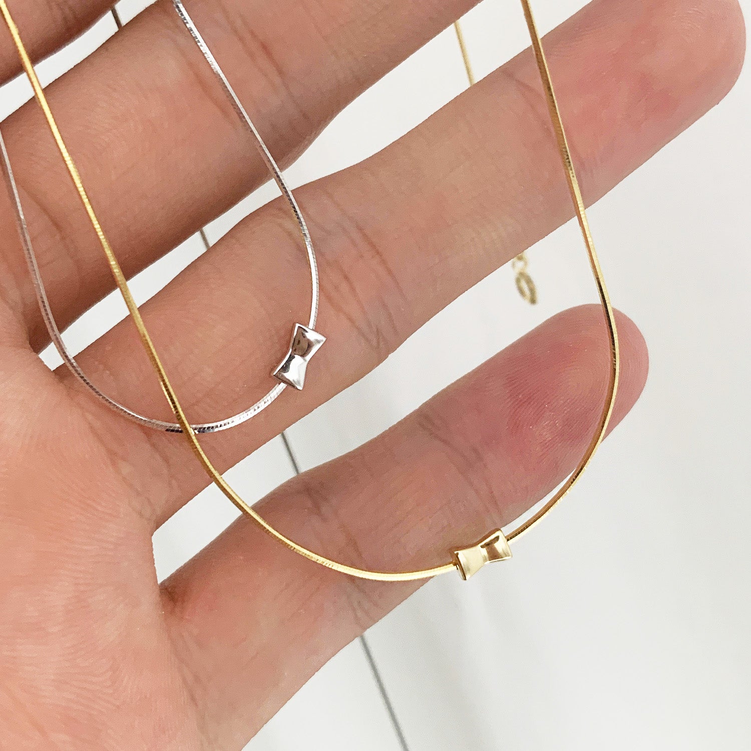 A set of 925 sterling silver mini bowknot herringbone necklaces, displayed in both gold and silver finishes on a neutral background.