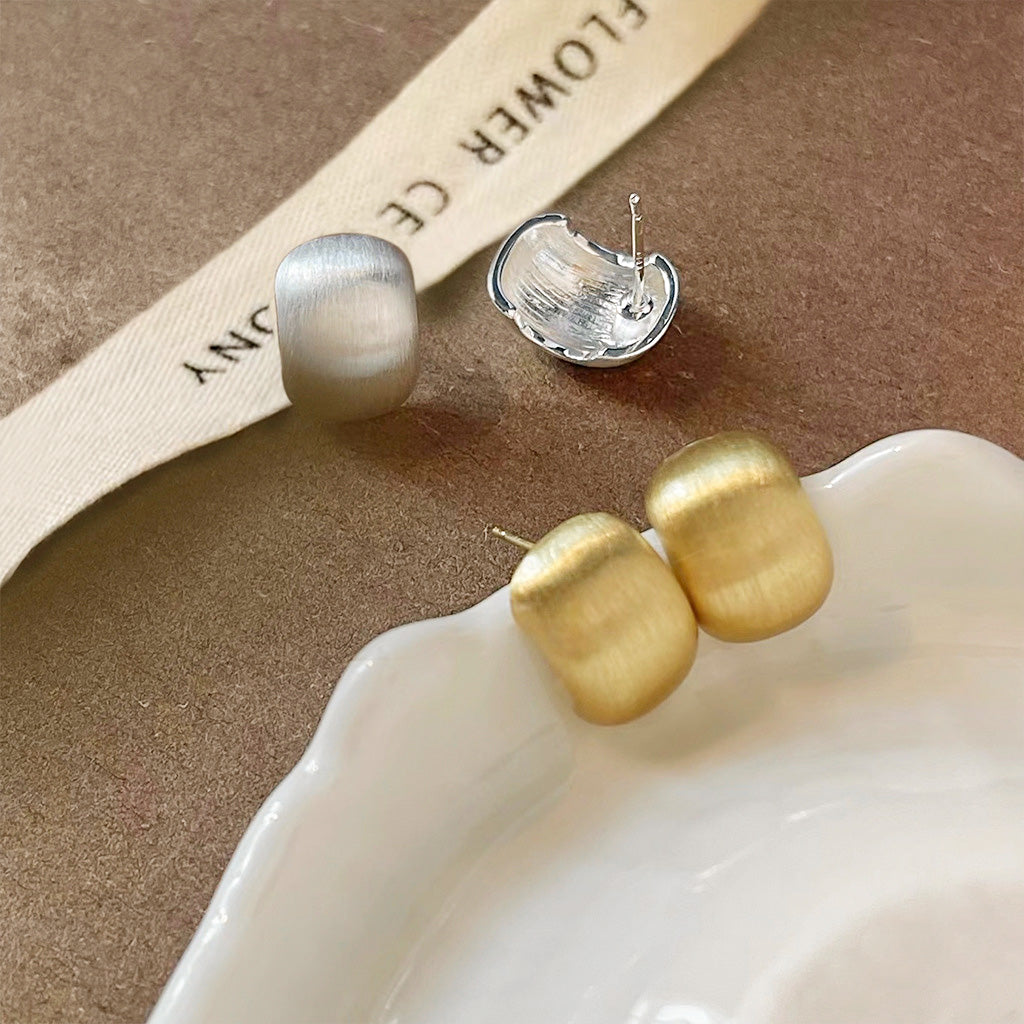 A set of simple French metal bead stud earrings in gold and silver finishes, displayed on a ceramic dish.