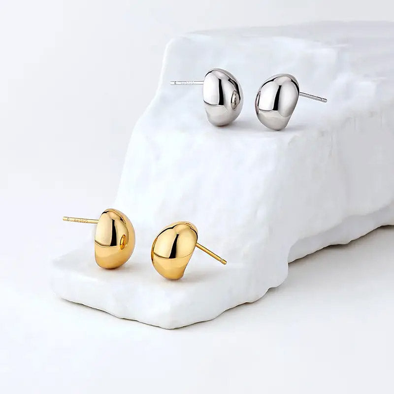 A pair of gold and a pair of silver 925 sterling silver French small bean stud earrings displayed on a white background, showcasing their minimalist design.