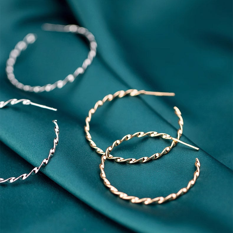 A collection of 925 sterling silver twist rope C hoop earrings in both gold and silver finishes, elegantly displayed on a textured teal fabric.
