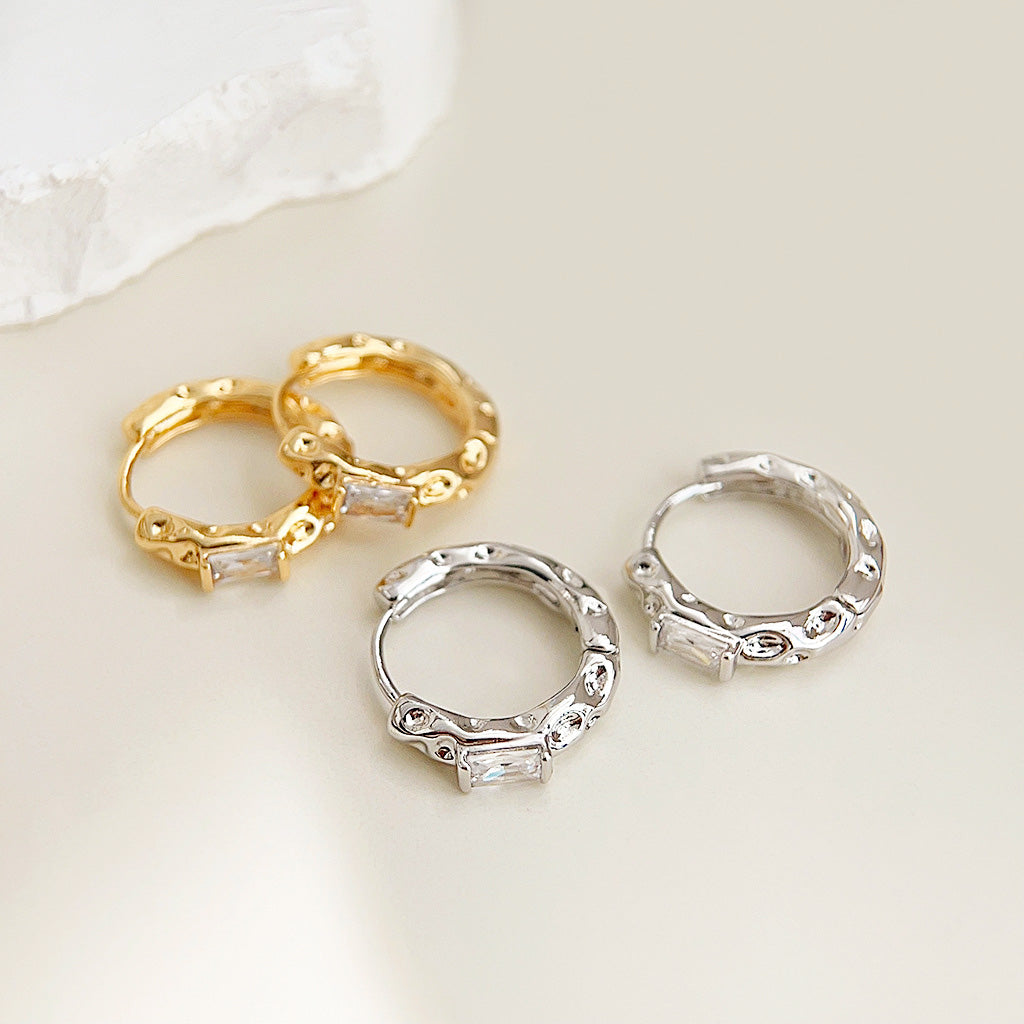 A set of hammered surface huggie hoop earrings in both gold and silver finishes, each featuring a rectangular zircon gemstone.