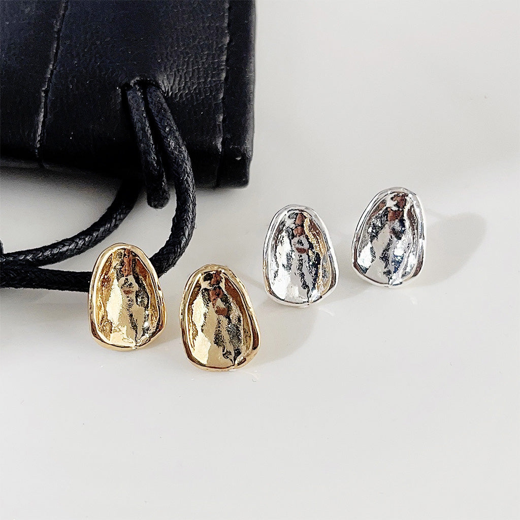 A set of simple oval button stud earrings in both gold and silver plating, displayed on a white surface next to a black branded pouch.