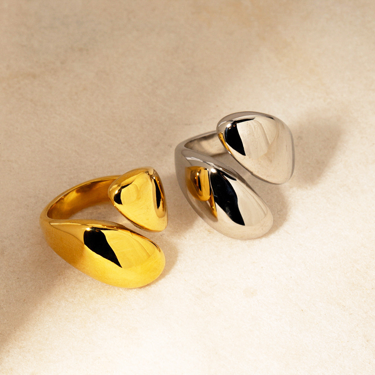 A set of modern, minimalist statement rings in polished gold and silver stainless steel, featuring a bold asymmetric design.