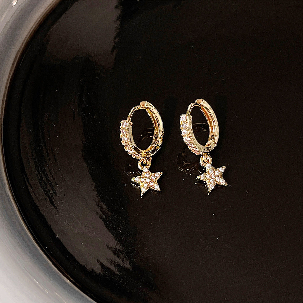 A pair of 14k gold plated brass huggie hoop earrings with sparkling cubic zirconia star drop charms, displayed on a white background.