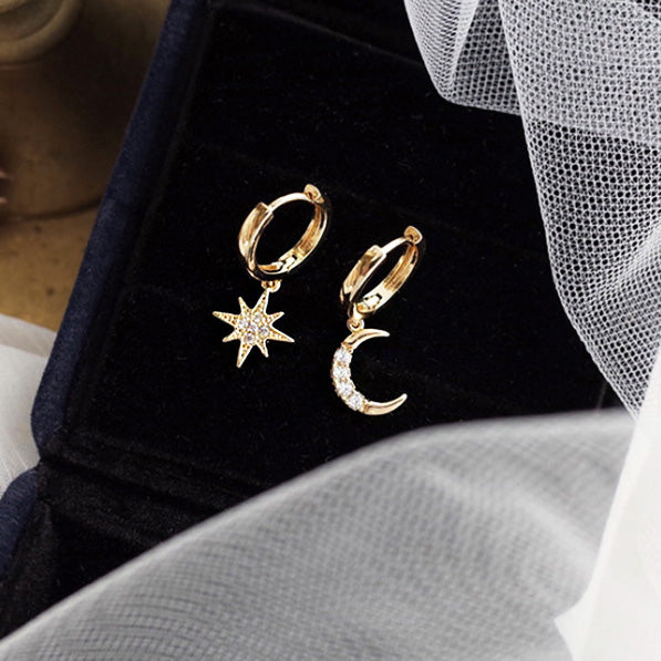 A set of 925 sterling silver star and moon huggie hoop earrings with gold plating, elegantly displayed in a black jewelry box.