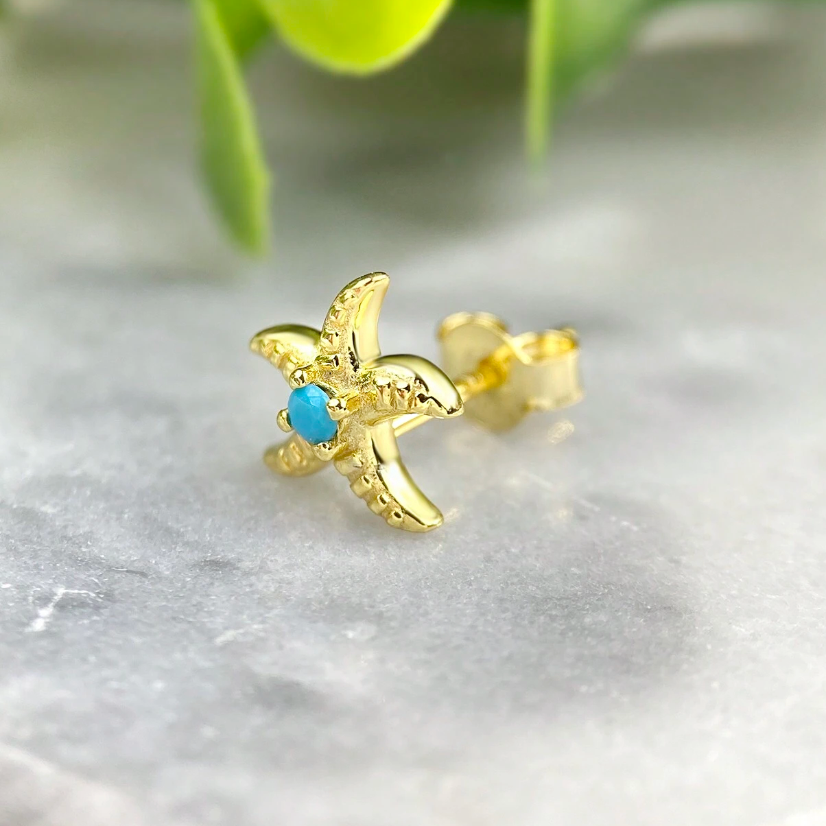 A detailed studio shot of a gold-plated 925 sterling silver starfish earring with a vibrant blue turquoise stone at its center.