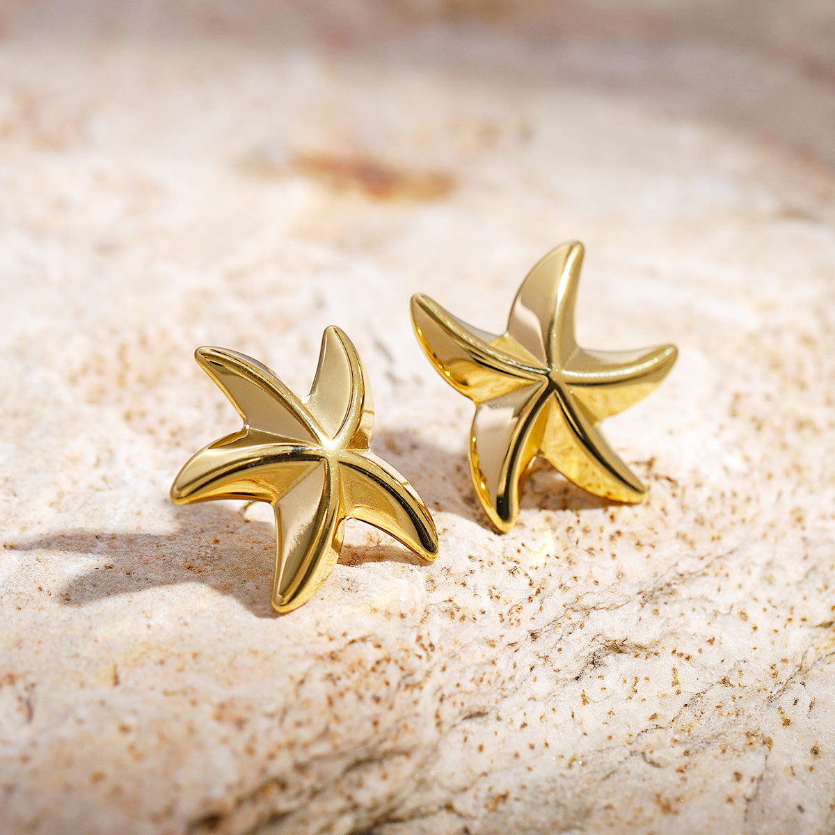 A pair of gold-plated stainless steel starfish stud earrings on a clean white background, representing waterproof beach jewelry.