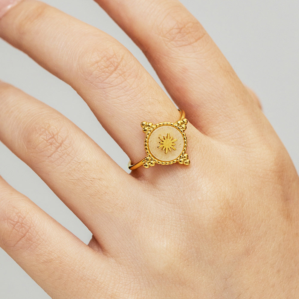 A close-up of a gold-plated stainless steel ring from a set of five, featuring an intricate sunburst design with a central pink crystal.