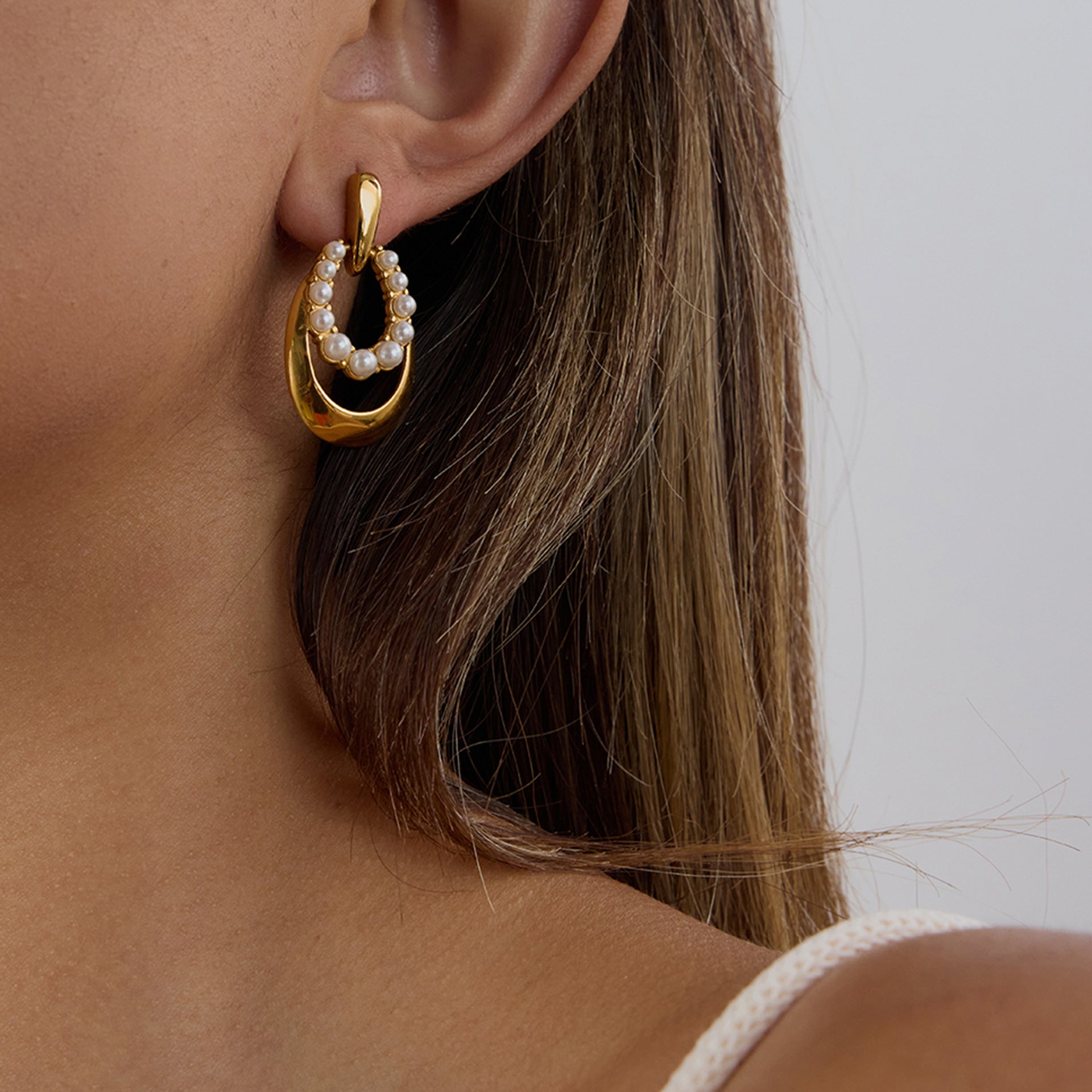 A woman wearing an elegant PVD gold-plated stainless steel pearl earring, showcasing its modern oval drop design and suitability for daily wear.