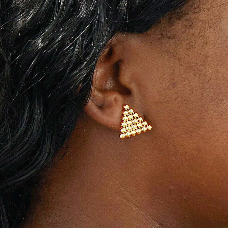 A close-up of a woman wearing the stainless steel gold round bead triangle stud earring, showcasing its detailed beaded texture.