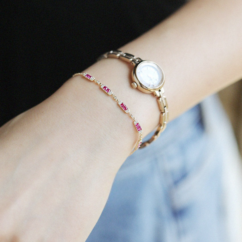A stylish 925 sterling silver charm bracelet with a pink ruby, elegantly worn on a wrist next to a gold watch, showcasing its versatile design.
