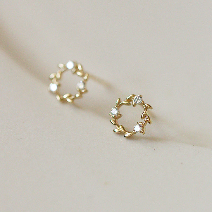 A close-up of the 925 sterling silver small gold wreath stud earrings, highlighting the intricate leaf design and sparkling white stones.