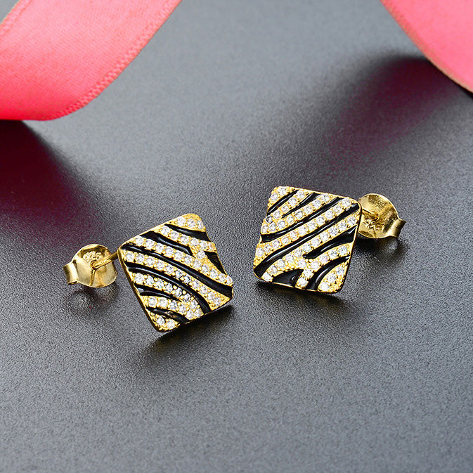 A pair of 925 sterling silver stud earrings with a striking gold-plated zebra pattern, embellished with small white stones, displayed on a white background.