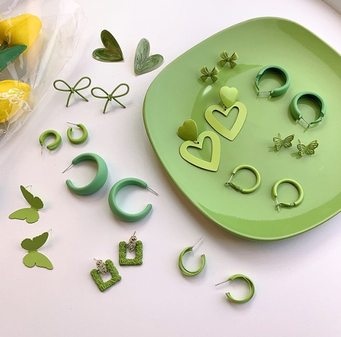 A vibrant collection of green enamel earrings from the Summer 2022 collection, showcasing various shapes and styles in alloy and brass.