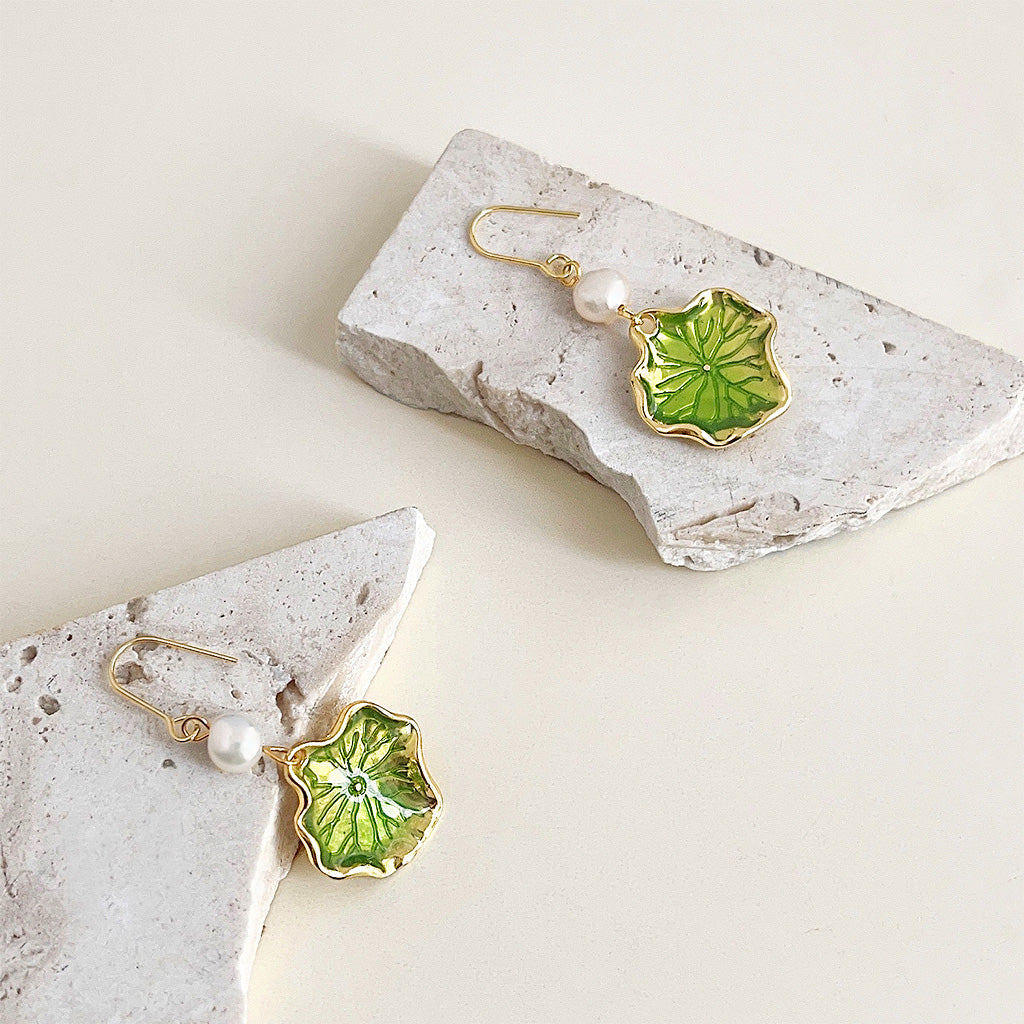 A stunning pair of 14k gold-plated earrings featuring green enamel lotus leaf pendants and dangling freshwater pearls, on a clean white background.
