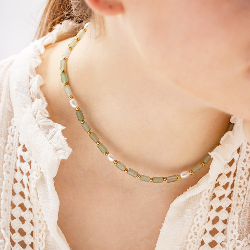 A close-up of a stainless steel boho necklace from a set of five, featuring greenish-gray natural stone beads, white pearls, and gold accents.