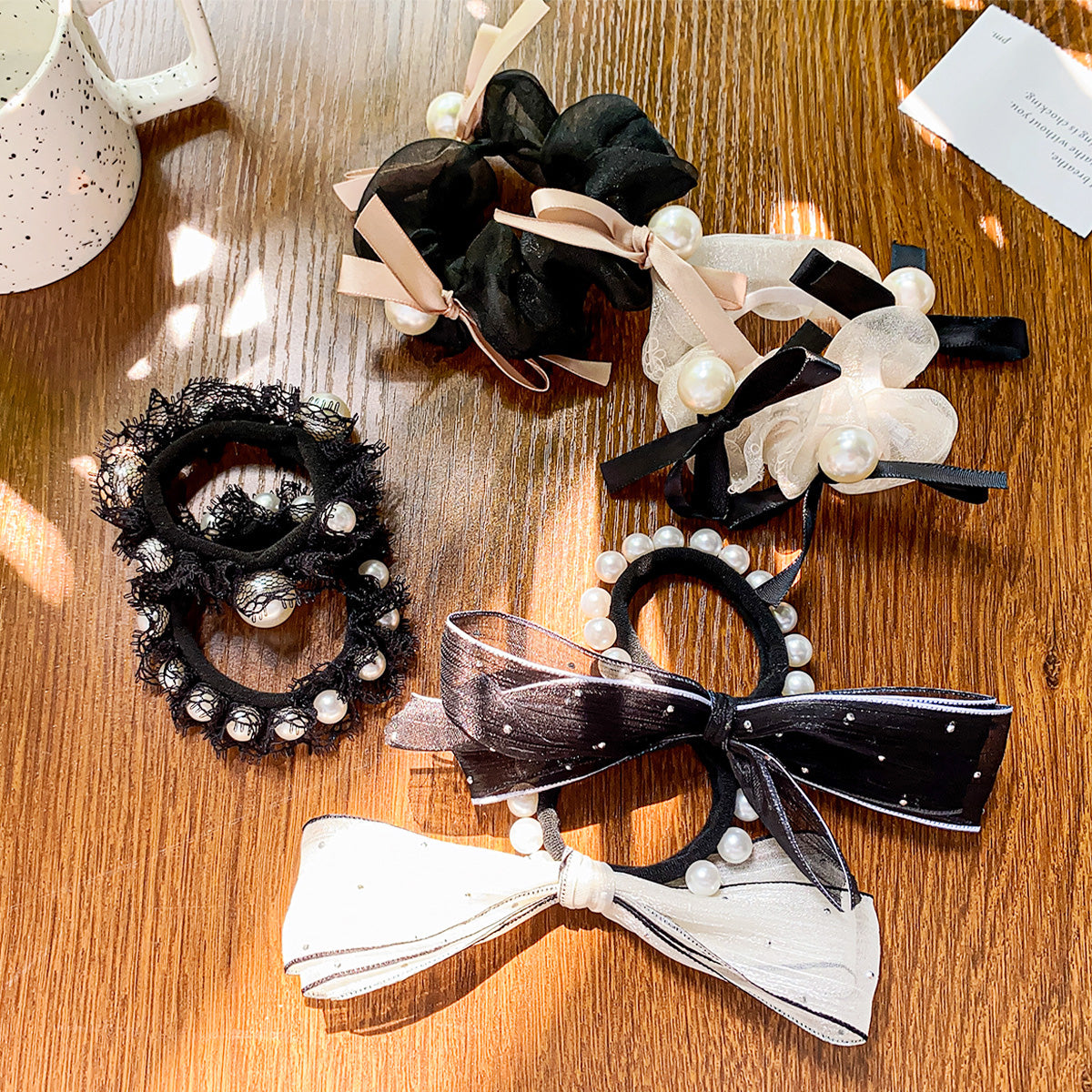 A collection of vintage-style hair accessories, including black and white lace bowknot hair ties and scrunchies embellished with elegant pearls and ribbons.
