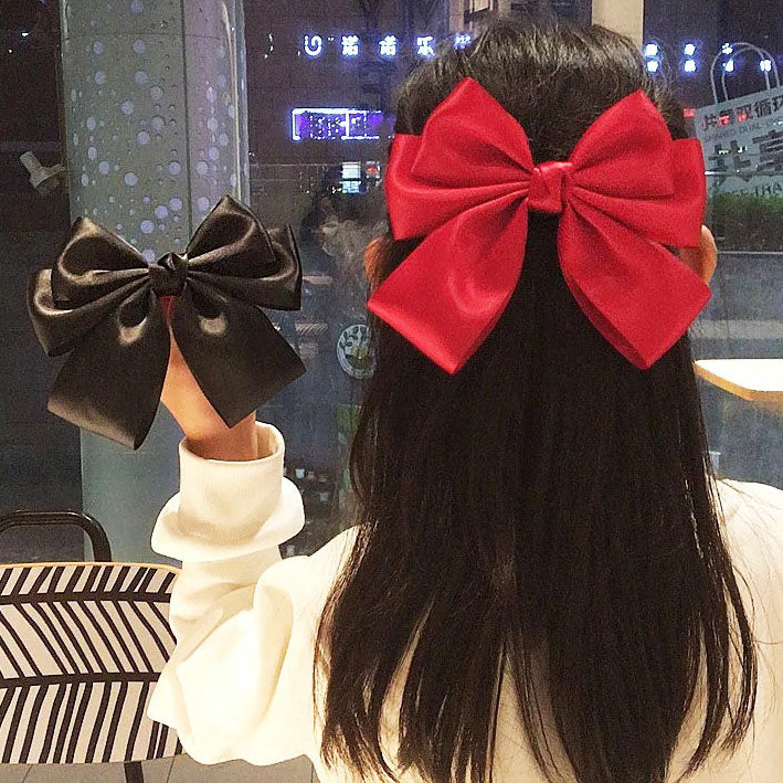 A model showcasing the vintage-style bowknot hair alligator clip, wearing a red bow in her ponytail and holding a black one.