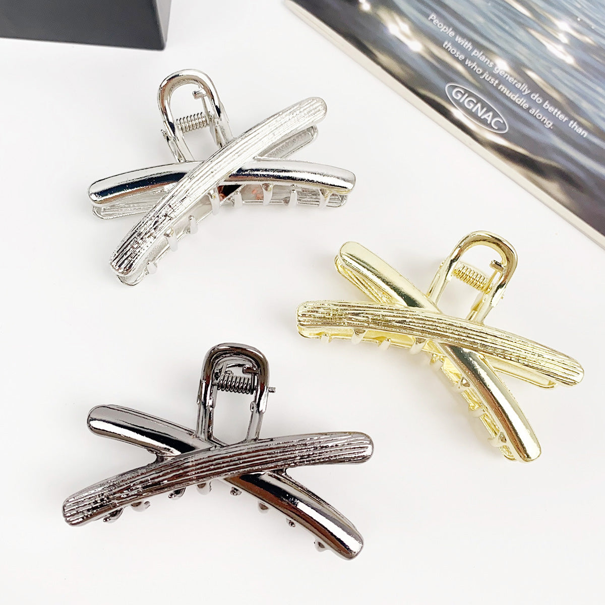 A trio of 7cm cross-hair claw clips in metallic gold, silver, and gun-black, showcasing their sleek design.