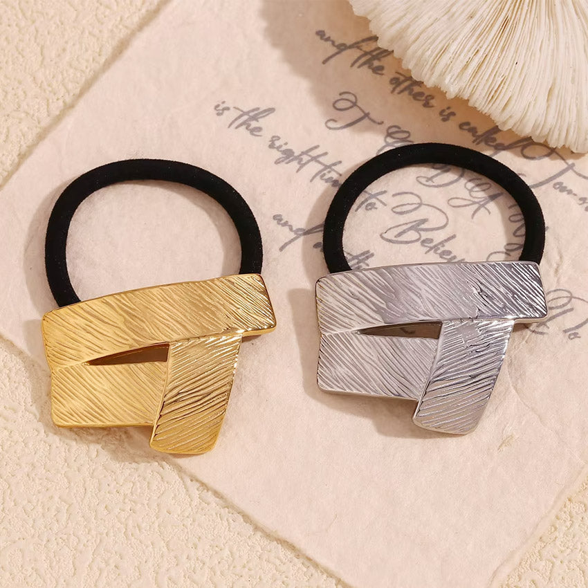 A pair of stainless steel geometric hair ties, one in a polished gold finish and the other in a sleek silver finish, displayed on a clean white background.