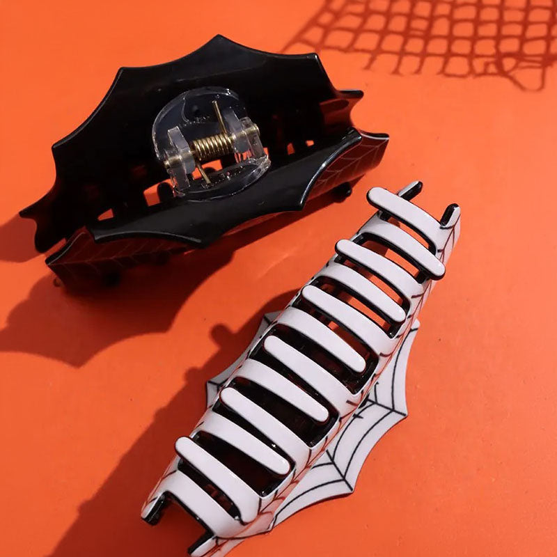 A pair of Y2K style hair claws, one black and one white, with Halloween-themed spider web designs.